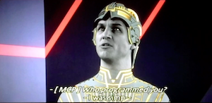 Closer head-and-shoulders screenshot of Clu 1 from TRON 1982. The subtitles still show the MCP asking: Who programmed you? and Clu responding: I was simp--