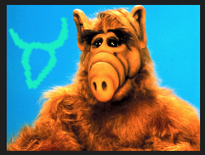 photo of Alf, a fuzzy alien character with pointy ears on the top of a head with a long muzzle. beside him is the Proto-Sinaitic version of the letter Aleph, which bears a resemblance to his head