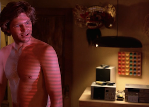 Flynn in his 1982 apartment, shirtless, with one of his rainbow decorations behind him