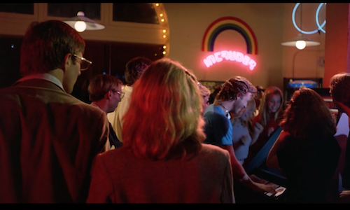 The scene where Alan and Lora found Flynn in his arcade. He is playing on a machine underneath a neon sign advertising a game called "Intruder," and the sign is rainbow-shaped.